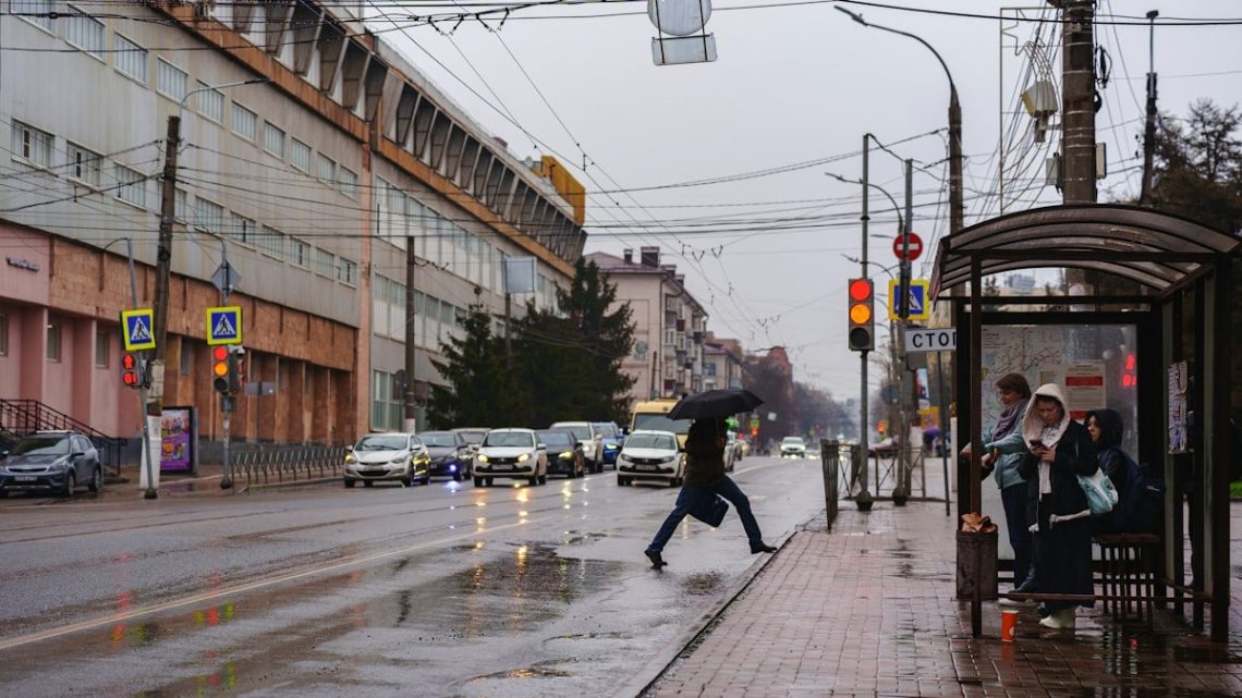 Pedestrian crosses street on rainy day at bus stop