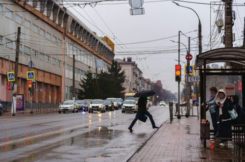 Pedestrian crosses street on rainy day at bus stop