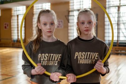 Twin girls in gym holding a hula hoop, wearing 'Positive Thoughts' sweatshirts.