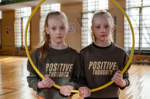 Twin girls in gym holding a hula hoop, wearing 'Positive Thoughts' sweatshirts.